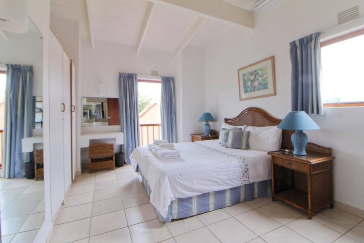 Une chambre à coucher comprenant un lit, deux tables de chevet avec des lampes, une commode, un miroir et une fenêtre avec des rideaux.