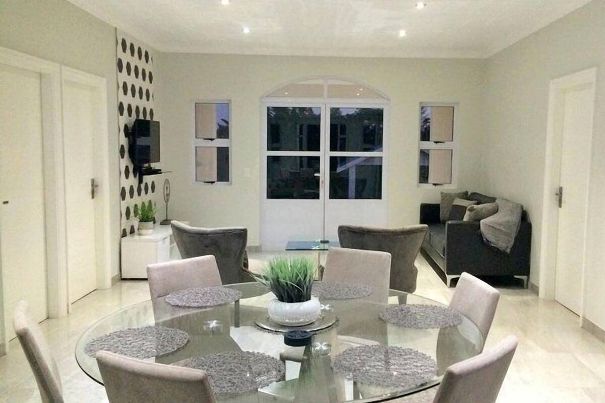 Une salle à manger moderne avec une table en verre, six chaises et une plante placée au centre.