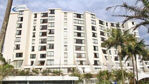 A multi-story hotel with a curved facade, a swimming pool, and palm trees. - Top Destinations (Southbroom)