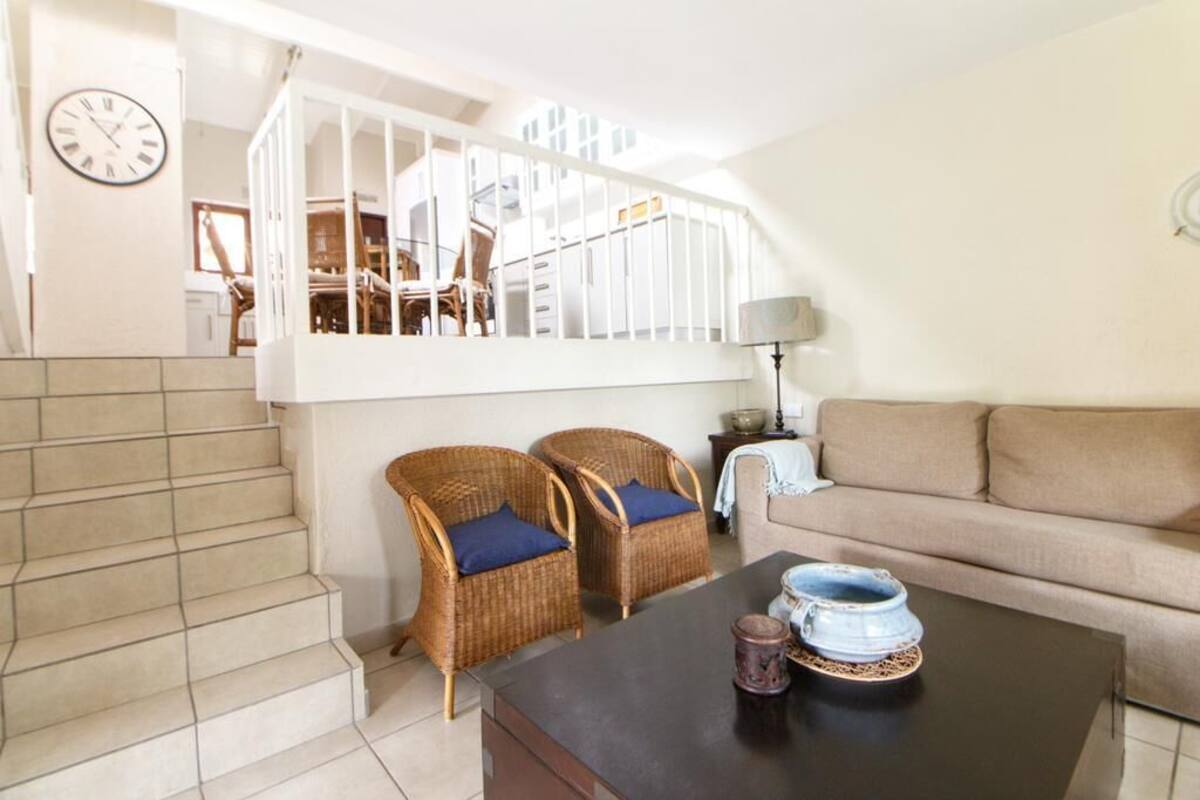 Un salon avec un escalier, des fauteuils en osier, un canapé, une table basse et une lampe.