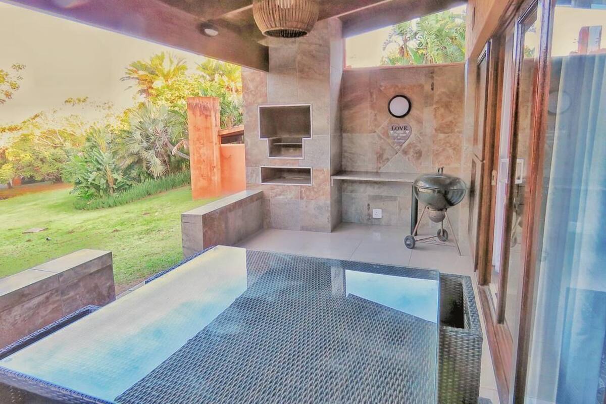 Une terrasse extérieure moderne, dotée d’une véranda en verre, d’un barbecue intégré et d’un mur en pierre sur lequel est inscrit le mot « AMOUR ».