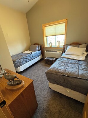 A room with two beds, a wooden dresser, a window with blinds, and a radiator.