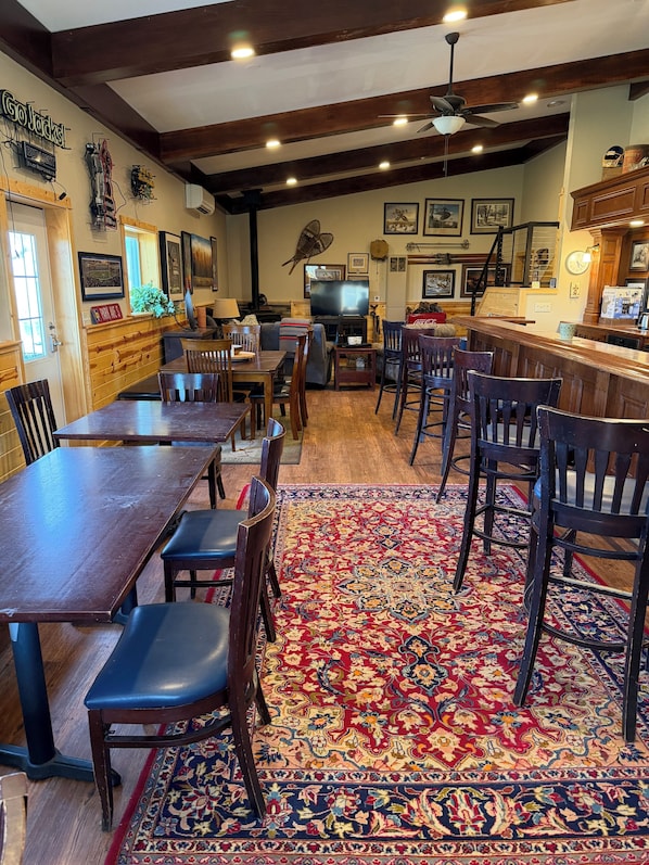 A cozy restaurant with wooden furniture, a bar area, and a large TV screen.