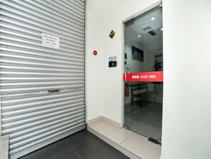 A hotel entrance with a closed metal shutter, a glass door with a red sign, and a fire extinguisher mounted on the wall. - OYO 89965 Stay Inn Ii (Kota Kinabalu)