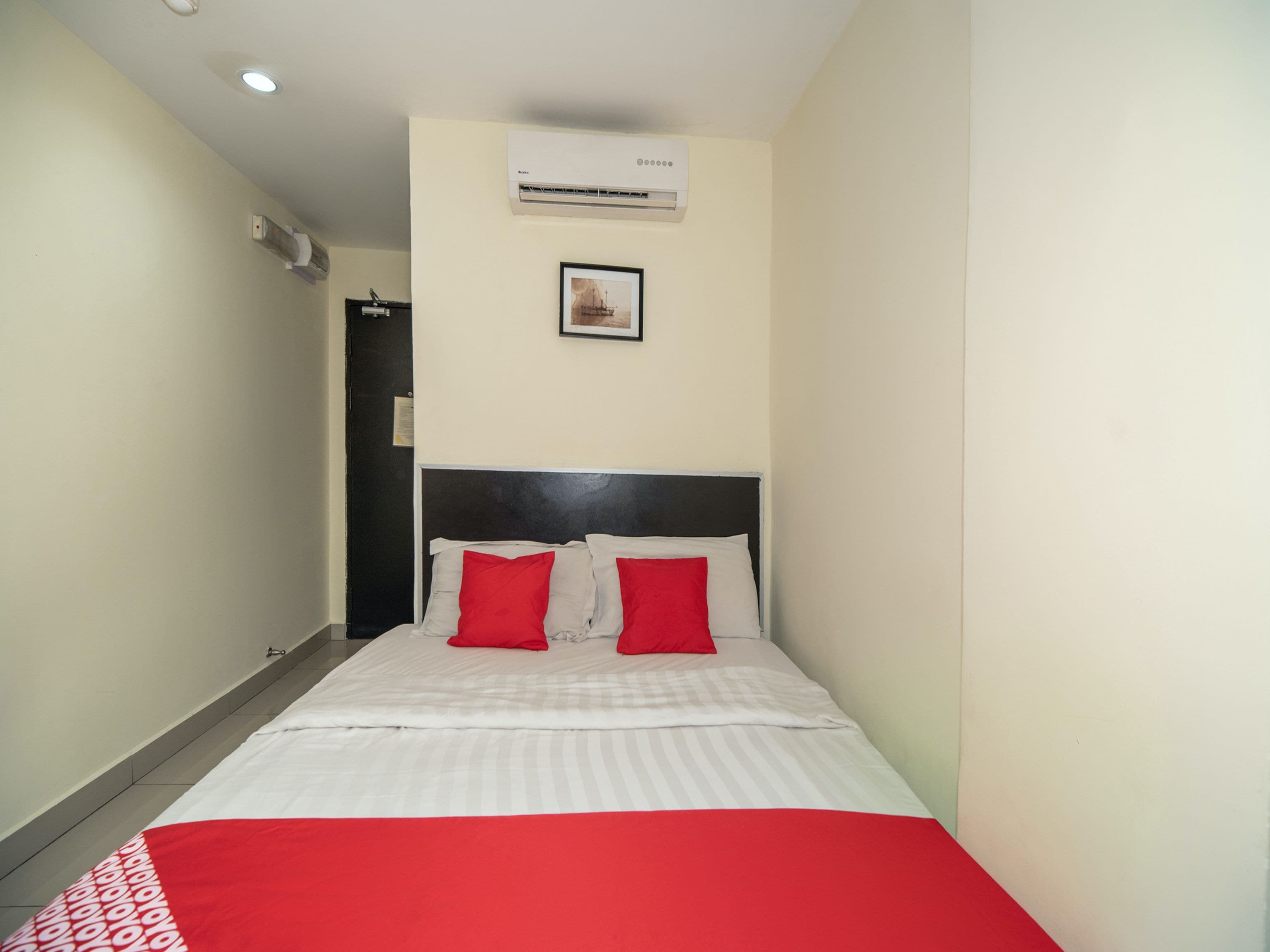 A hotel room with a bed, a framed picture on the wall, and an air conditioning unit.