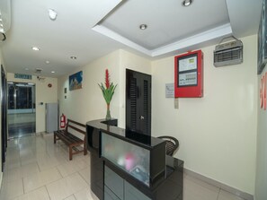 A reception area with a reception desk, a bench, a potted plant, a door, and a wall-mounted control panel. - OYO 89965 Stay Inn Ii (Kota Kinabalu)