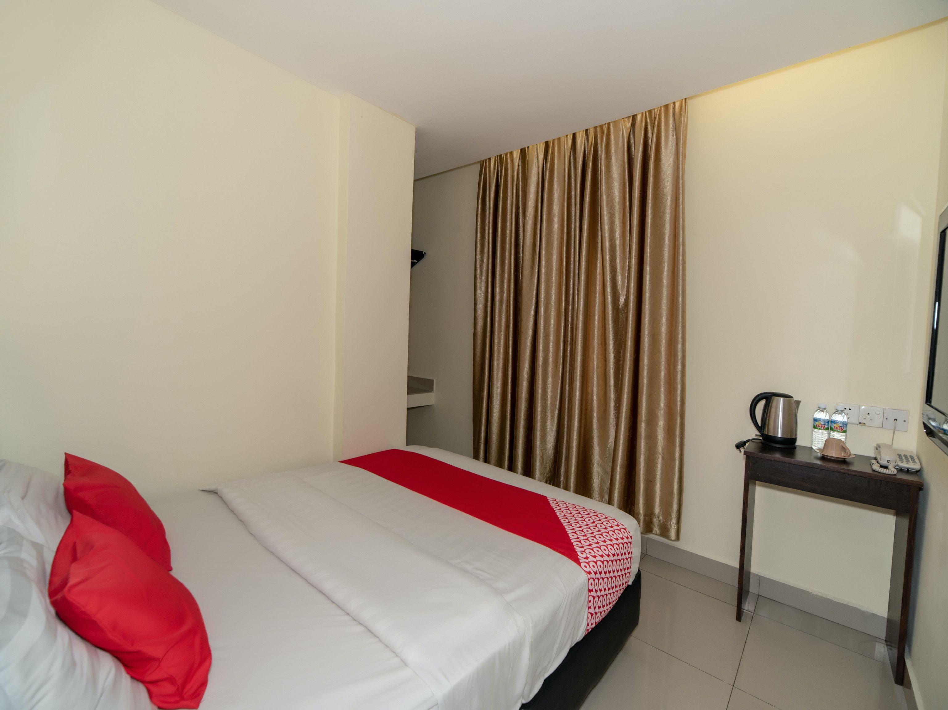 A hotel room with a bed, a bedside table with a kettle, and a mirror.