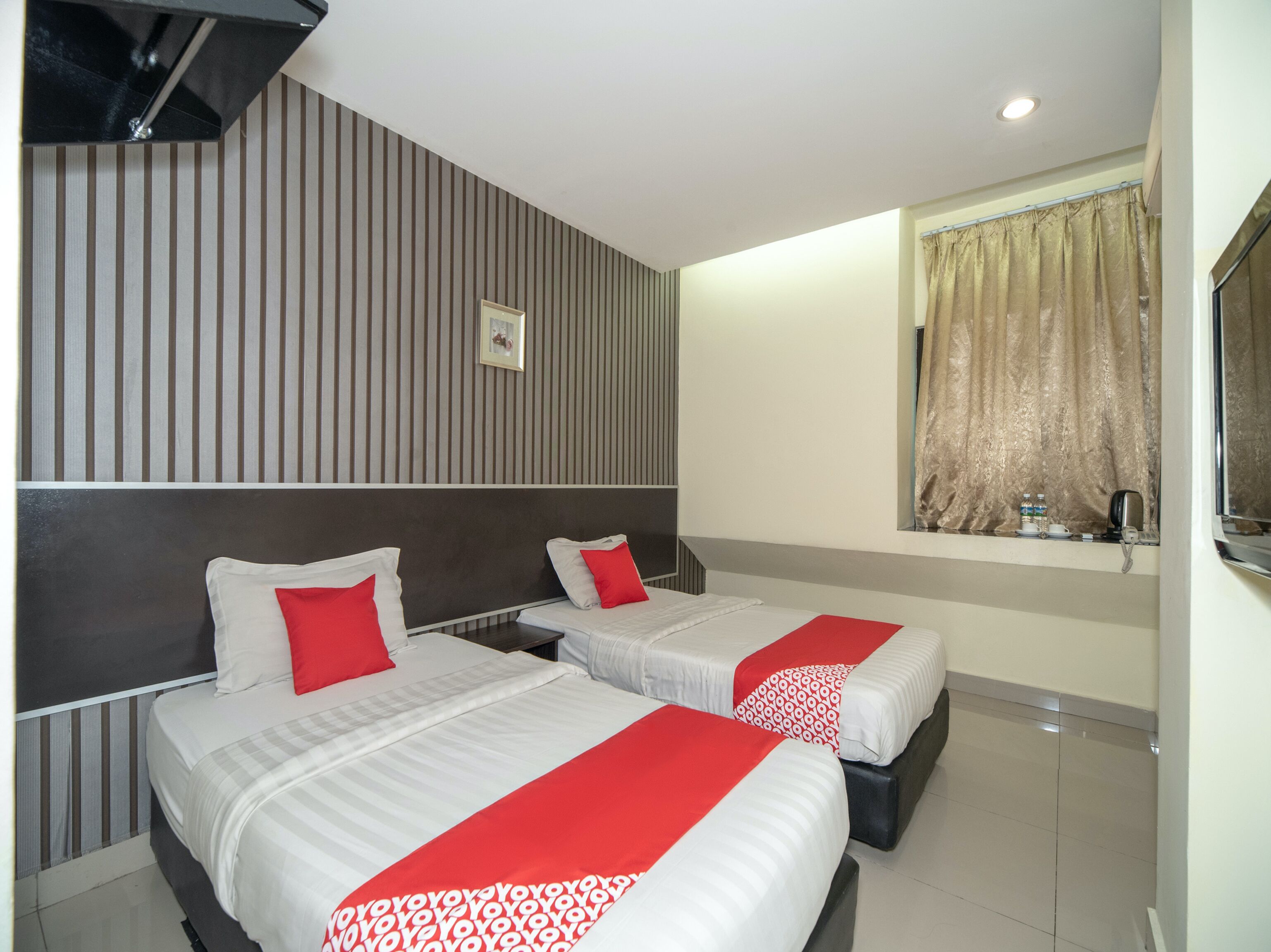 A hotel room with two beds, a window with curtains, a small table with a kettle, and a picture on the wall.