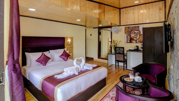 A hotel room with a large bed, a desk with a chair, a Buddha statue, and a TV.