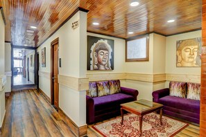 A hallway with wooden flooring, purple sofas, a glass coffee table, and Buddha paintings on the walls. - Sumitel Sanderling, Darjeeling (Darjeeling)