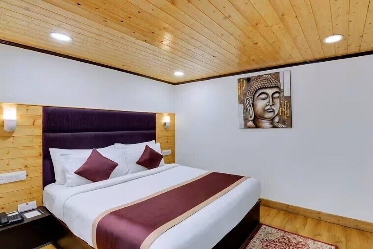 Un dormitorio con techo de madera, cama con ropa de cama blanca y burdeos, una obra de arte colgada en la pared y una pared de acento de piedra.