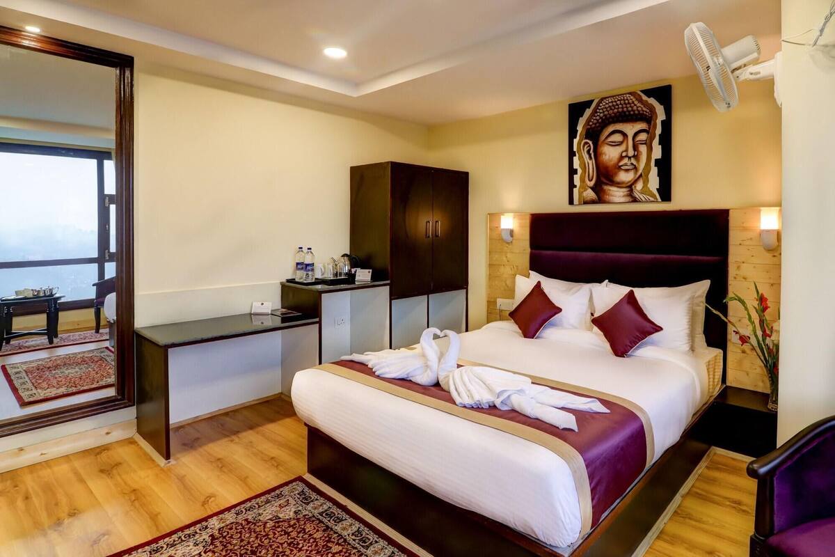 Habitación de hotel con cama, escritorio, espejo, pintura de Buda y vistas.