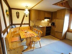 A compact kitchen with wooden cabinets, a tiled backsplash, a dining table with chairs, and a hanging light fixture. - Fontauna Degonda, (Sedrun), 235.01 by Interhome (Sedrun)