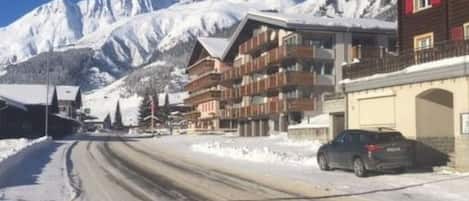 A snow-covered road with buildings and mountains in the background.