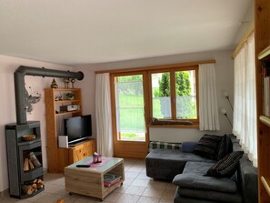 Ein gemütliches Wohnzimmer mit Kamin, Fernseher, Sofa und einem Vorhangfenster.