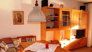 Una sala de estar acogedora con un sofá de madera, una mesa de comedor con una vela roja y un televisor sobre un mueble de madera.