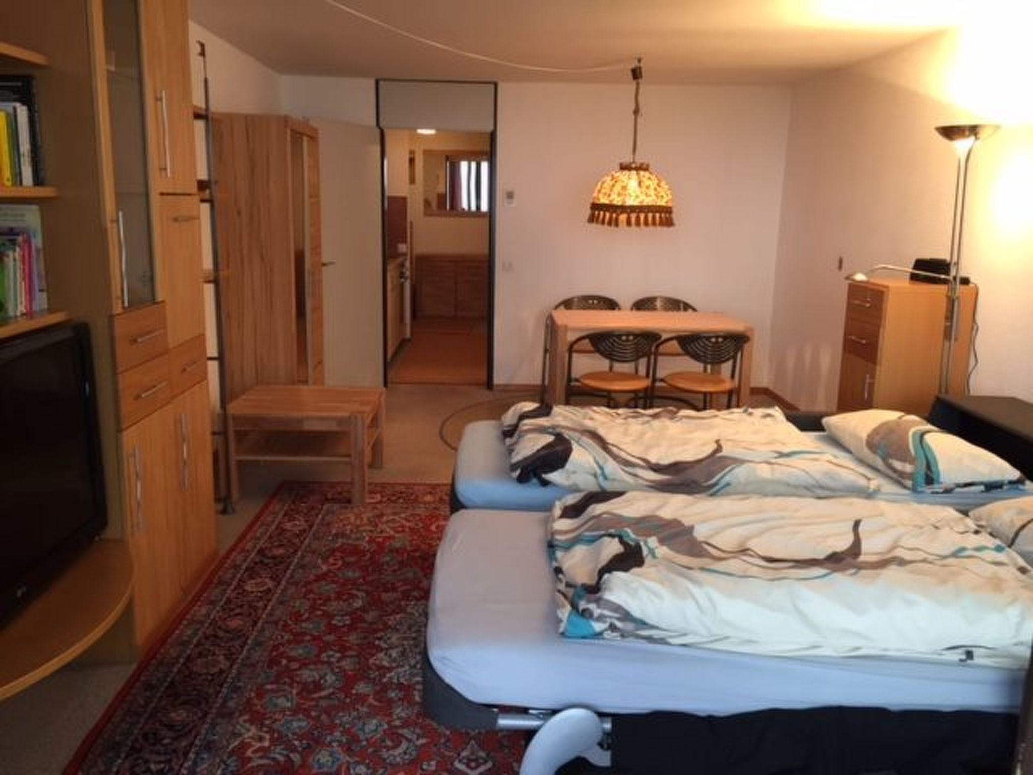 Ein kleines Hotelzimmer mit einem Bett, einem Schreibtisch, einem Sessel, einem Fernseher und einem Kleiderschrank.