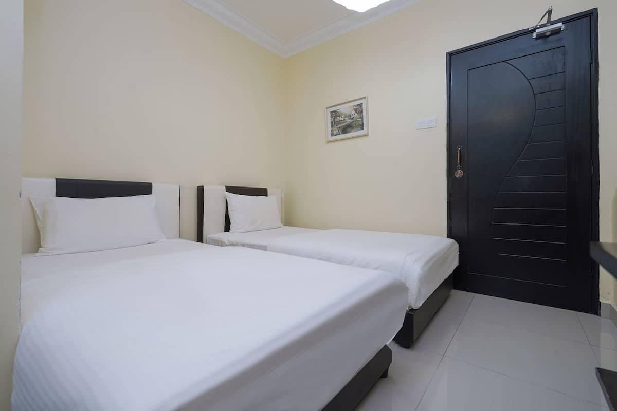 Ein Hotelzimmer mit zwei Einzelbetten, einer schwarzen Tür, einem kleinen gerahmten Bild an der Wand und einer Deckenleuchte.