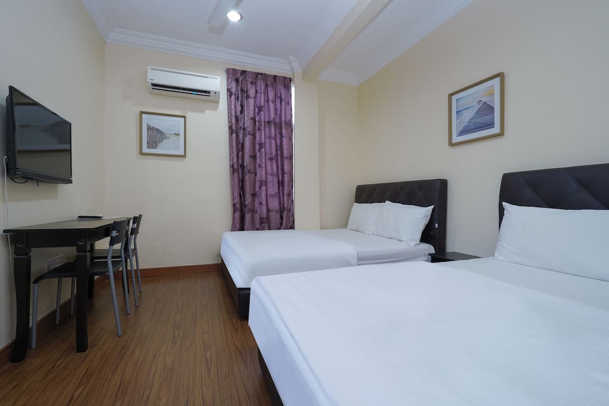 Ein Hotelzimmer mit zwei Betten, einem Schreibtisch, einem Stuhl, einer Klimaanlage, einem Fernseher und einem gerahmten Bild an der Wand.