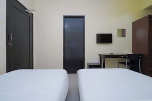 Quarto com duas camas, uma escrivaninha, uma cadeira, uma televisão e um guarda-roupa.