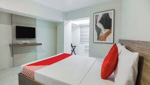 A modern hotel room with a large bed, a flat-screen TV mounted on the wall, a wooden bedside table, and a framed abstract artwork.