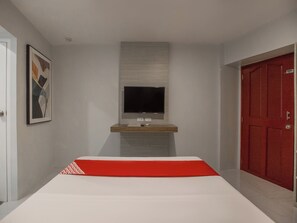 A modern hotel room with a bed, a mounted TV, a red door, and a framed picture on the wall. - OYO 675 Circuit Hostel (Makati)