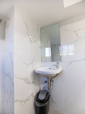 A bathroom with a white marble sink, a mirror, and a trash bin.
