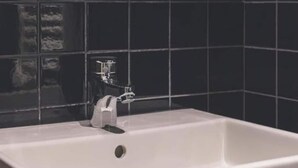 A bathroom with a white bathtub, a faucet, and black tiled walls.
