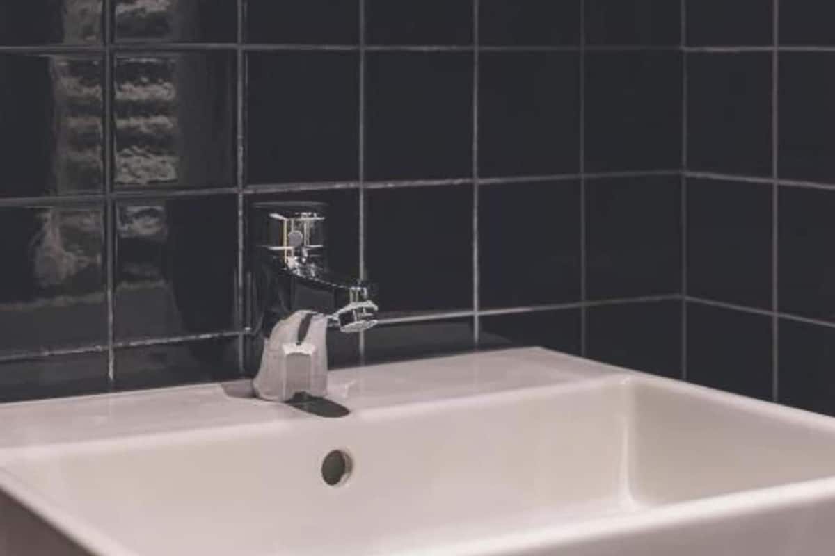 A bathroom with a white bathtub, a faucet, and black tiled walls.