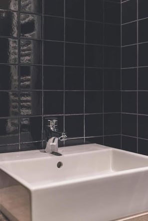 Un baño con una bañera blanca, un grifo y paredes cubiertas de azulejos negros.