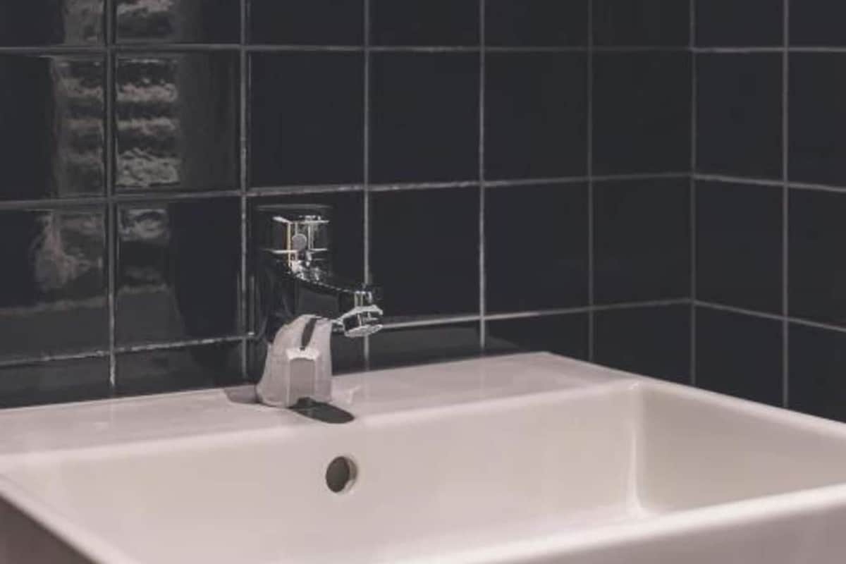 Un baño con una bañera blanca, un grifo y paredes cubiertas de azulejos negros.
