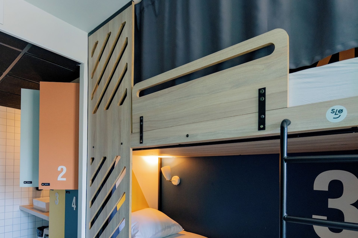 Una cama individual con cabecera de madera, un escritorio y una silla en una habitación con piso de baldosas.