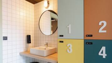 Un baño con lavamanos, espejo y taquillas numeradas.