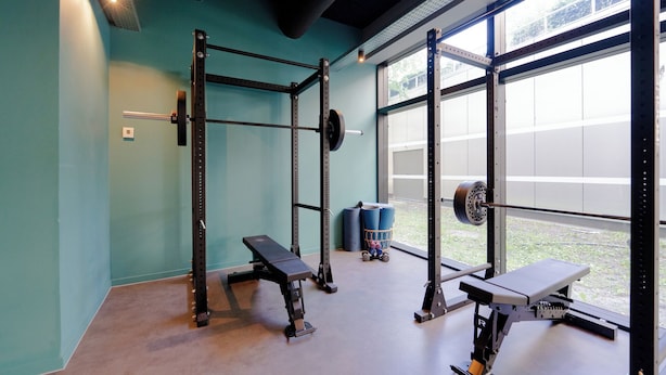 Un gimnasio con equipamiento para levantar pesas, bancos y un amplio ventanal.
