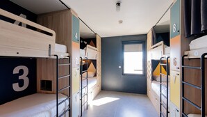 Una camera in stile dormitorio con letti a castello, armadietti numerati e una finestra che lascia entrare la luce naturale.