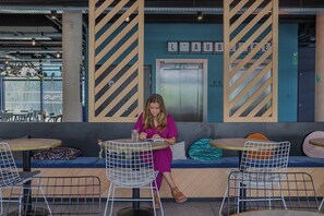 Mulher lendo à mesa em café moderno com parede azul e painéis listrados.