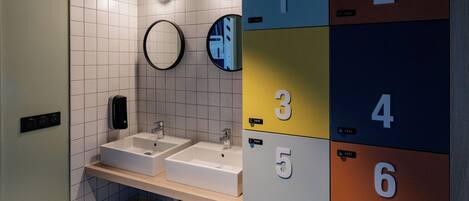 A modern bathroom with two sinks, a mirror, and lockers numbered 1 to 8.