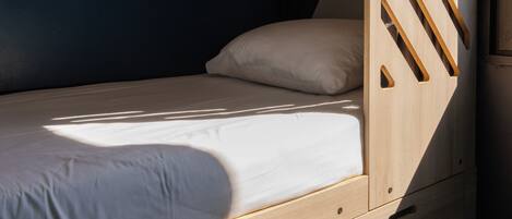 A bunk bed with a wooden ladder, a single bed with a white pillow, and a small desk with drawers numbered 1 and 2.