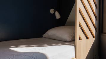 A bunk bed with a wooden ladder, a single bed with a white pillow, and a small desk with drawers numbered 1 and 2.