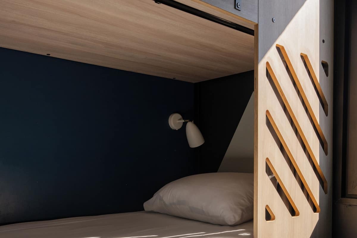 A bunk bed with a wooden ladder, a single bed with a white pillow, and a small desk with drawers numbered 1 and 2.