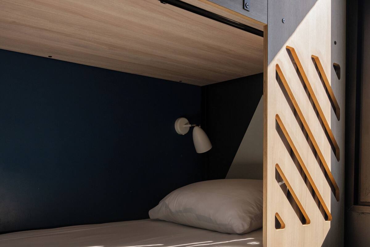 A bunk bed with a wooden ladder, a single bed with a white pillow, and a small desk with drawers numbered 1 and 2.