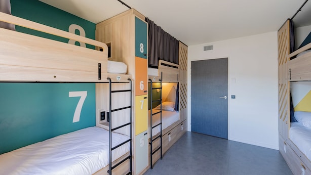 Une petite chambre de dortoir équipée de lits superposés, d’une porte et d’un petit placard.