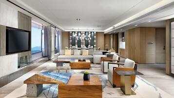 A modern hotel lobby with a large sofa, wooden coffee tables, and a flat-screen TV mounted on the wall.