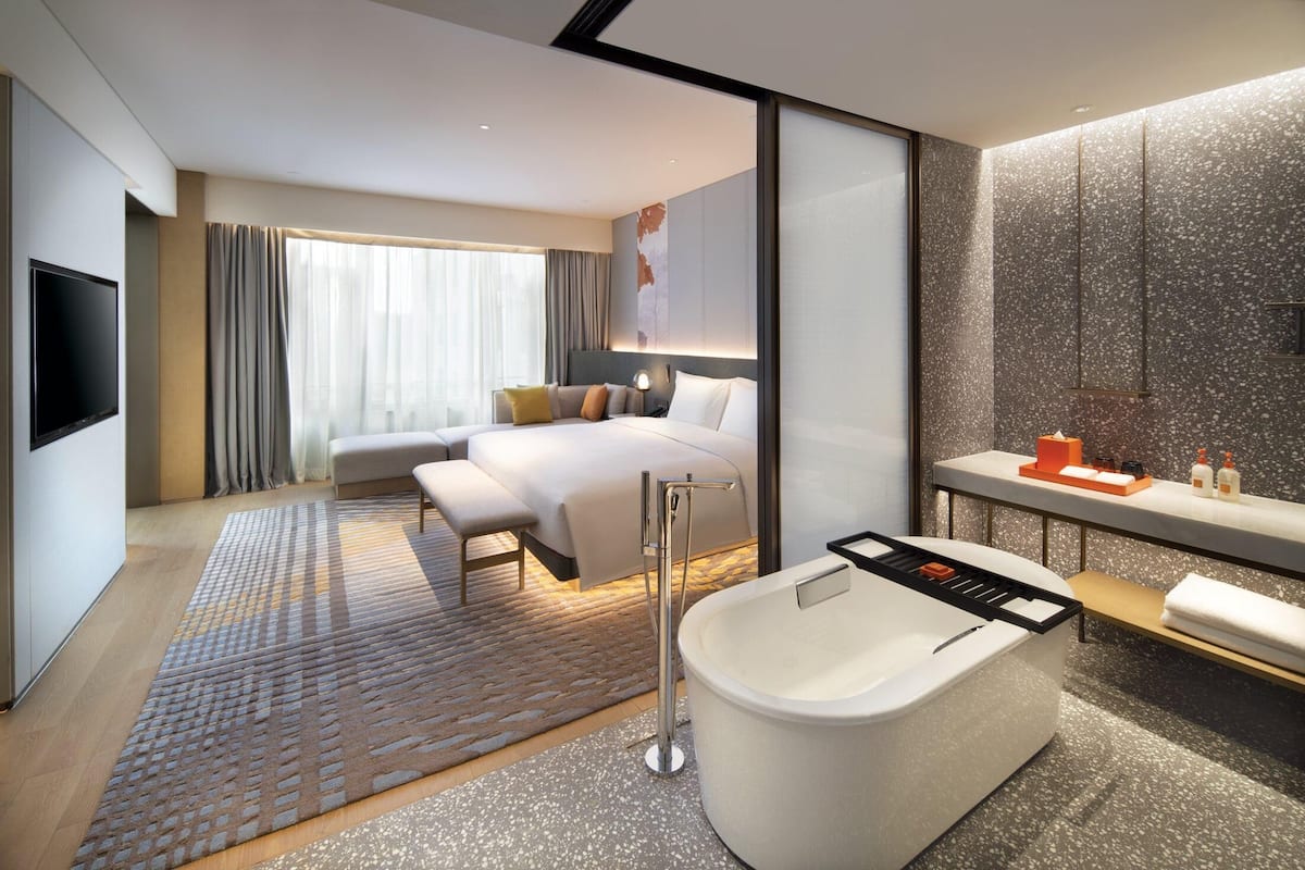 Una habitación de hotel moderna con una cama grande, un área de estar separada, una bañera y un televisor.