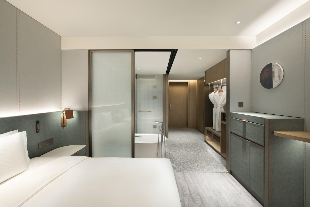 Een moderne hotelkamer met een groot bed, een inloopkast, een badkamer met een bad en een douche.