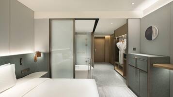 Una habitación de hotel moderna con una cama grande, un vestidor amplio, un baño con bañera y ducha.