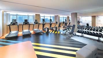 Ein Fitnessraum mit Laufbändern, Crosstrainern und einer Hantelbank.