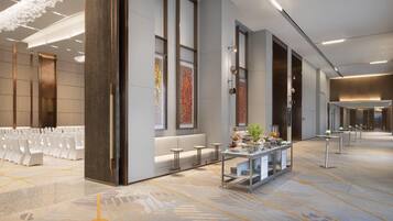 A spacious hotel lobby with rows of white chairs, a reception desk, and a decorative wall with patterned artwork.
