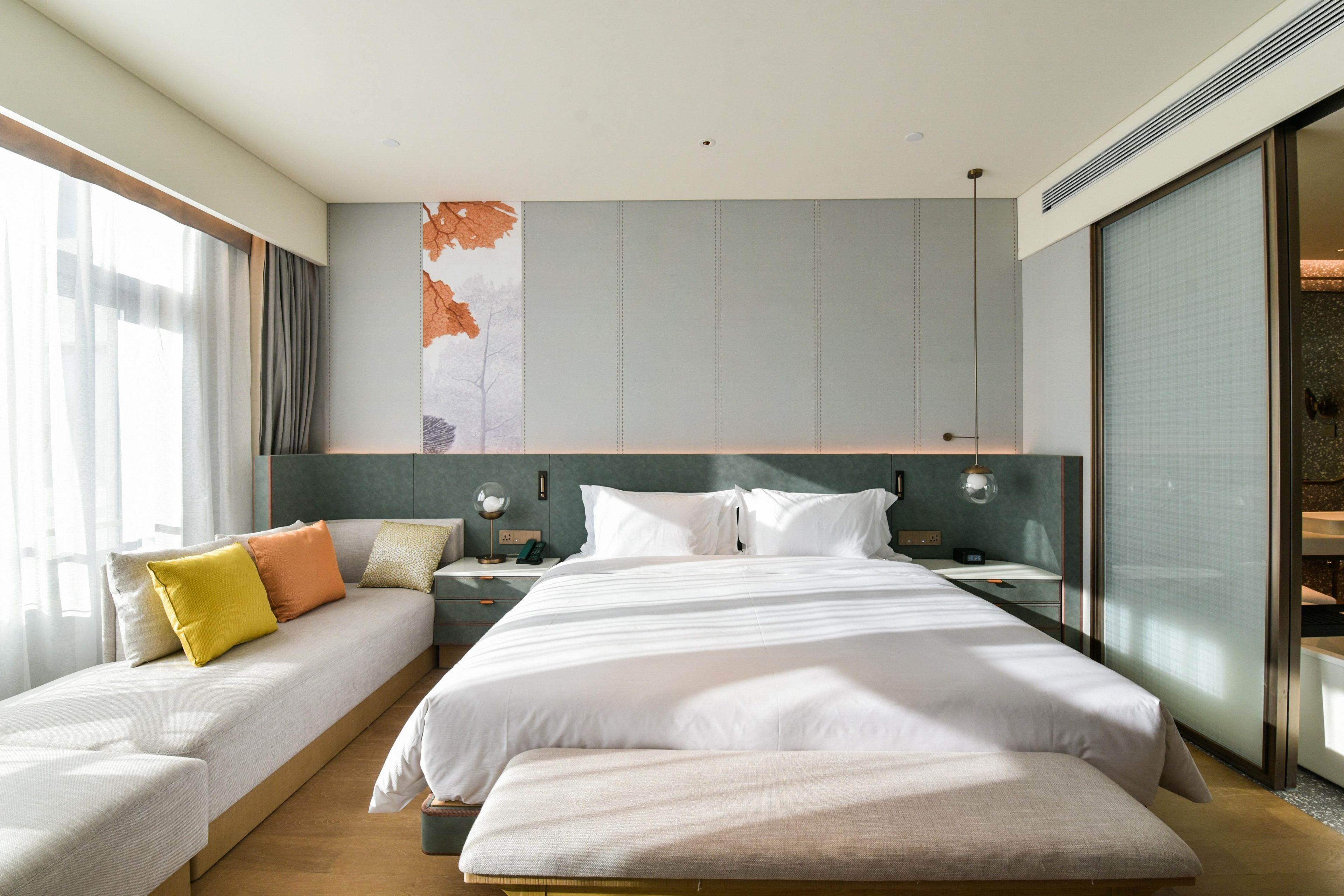 A modern hotel room with a large bed, a sofa bed, a bedside table, and a large window.