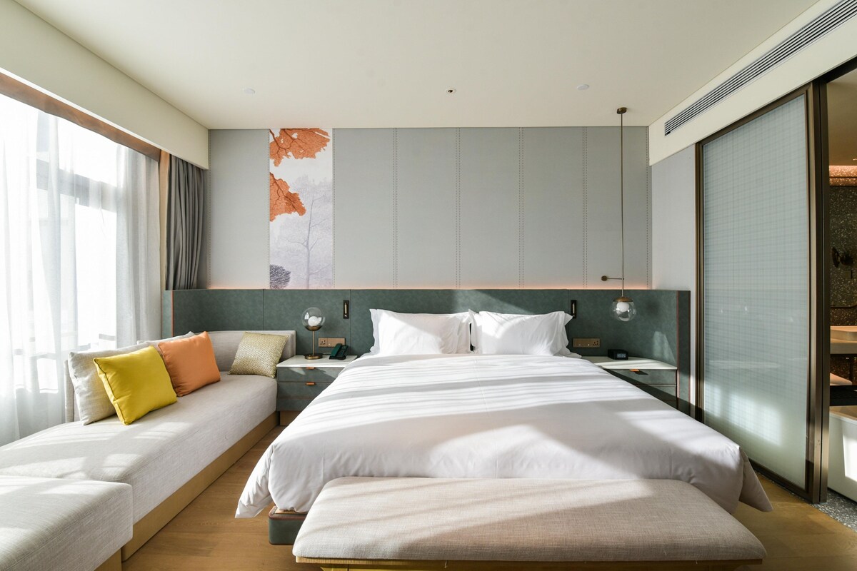 Een moderne hotelkamer met een groot bed, een slaapbank, een nachtkastje en een groot raam.